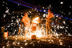 Two iron workers surrounded by sparks during an iron pour.