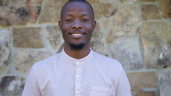 Olivier Mbabazi standing in front of a stone wall