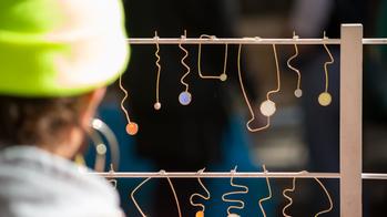 A person in a green hat looks at a rack of wire crafts. 