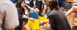 several students look at and discuss a small yellow chair during a studio critique