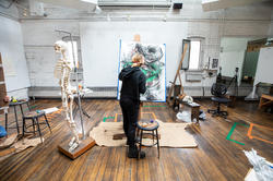 risd student in a brightly lit classroom facing their drawing next to a skeletal model