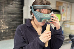 a student wearing an opera visor closely inspects a platinum ring she is working on