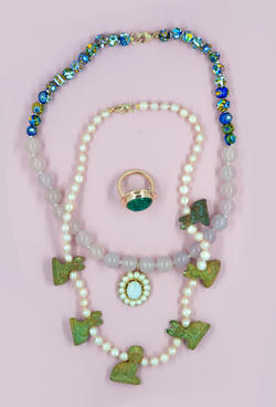 Two beaded necklaces and a ring against a pale purple background.