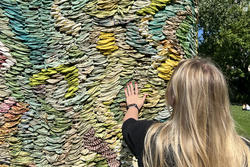 A person with long blond hair reaches out and touches a colorful sculpture