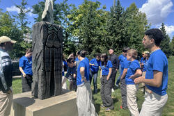 A group stands outside and views a sculpture in a park