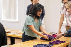 a student lifts and observes textile samples on a studio table as others look on