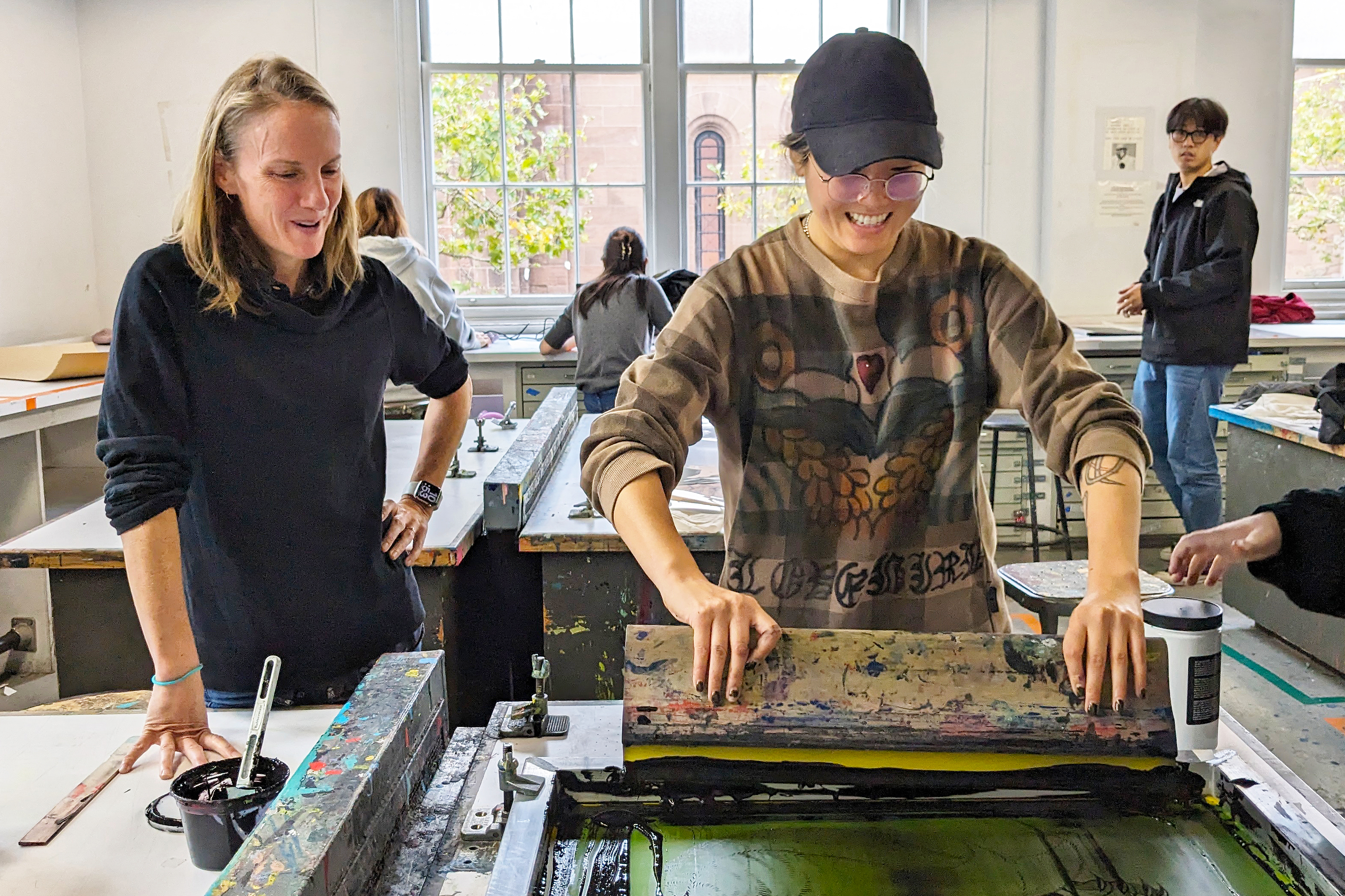 Megan Foster looks on as Tori Hong uses a squeegie to pull a print