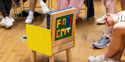 a colorful chair inspired by Legos sits at the center of a circle of students and guest critics