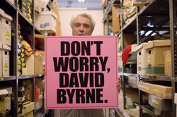 musician David Byrne holds up a sign that says Don't Worry