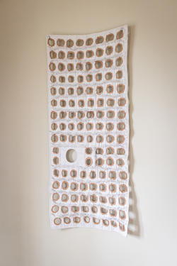 a brittle-looking long textile with many evenly round holes hangs from a wall